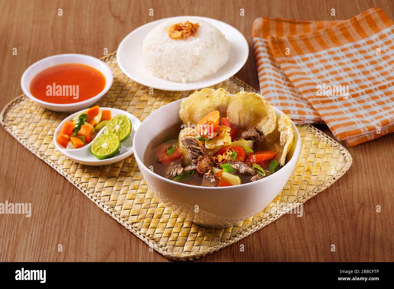 Indonesische traditionelle Rindfleischsuppe mit Reis, Gurken, Chips und Chilisauce Stockfoto
