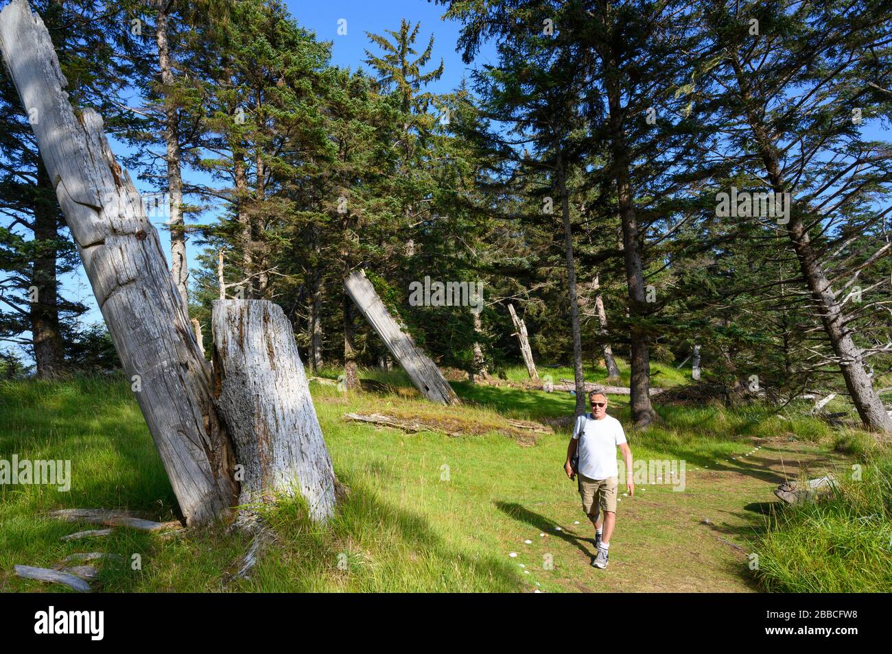 Besucher erkunden die alten Haida-Polen bei Skedans, auch bekannt als Koona oder Ḵ'uuna Llnagaay, Haida Gwaii, früher bekannt als Queen Charlotte Islands, British Columbia, Kanada Stockfoto