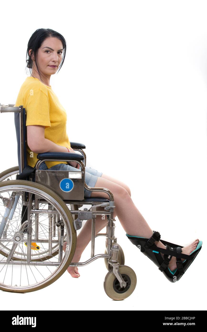 Legere mittlere Erwachsene Frau im Rollstuhl mit Fußorthosis isoliert auf weißem Hintergrund Stockfoto