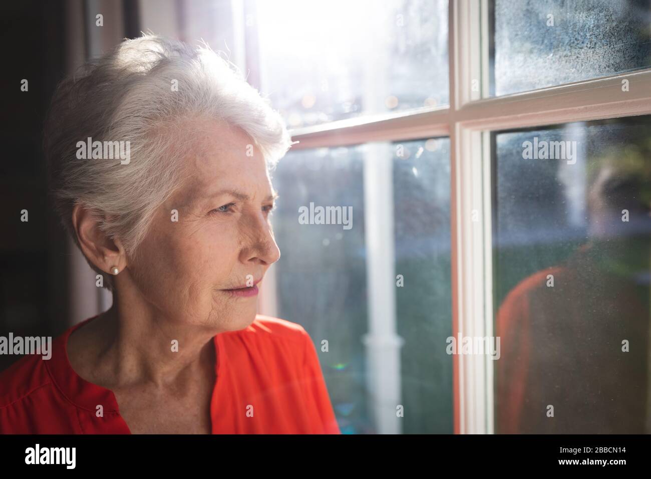 Kaukasische Seniorin, die zu Hause über das Fenster blickt Stockfoto