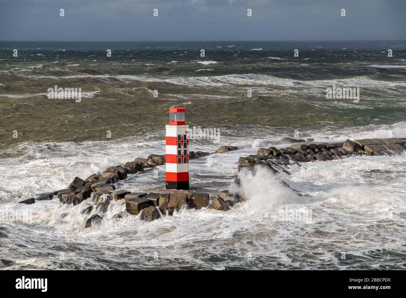 Raue Meere am rot-weißen Leuchtturm am Pier von IJmuiden, an der Einmündung des Nordseekanals, Noordpier, Reyndersweg Niederlande Stockfoto
