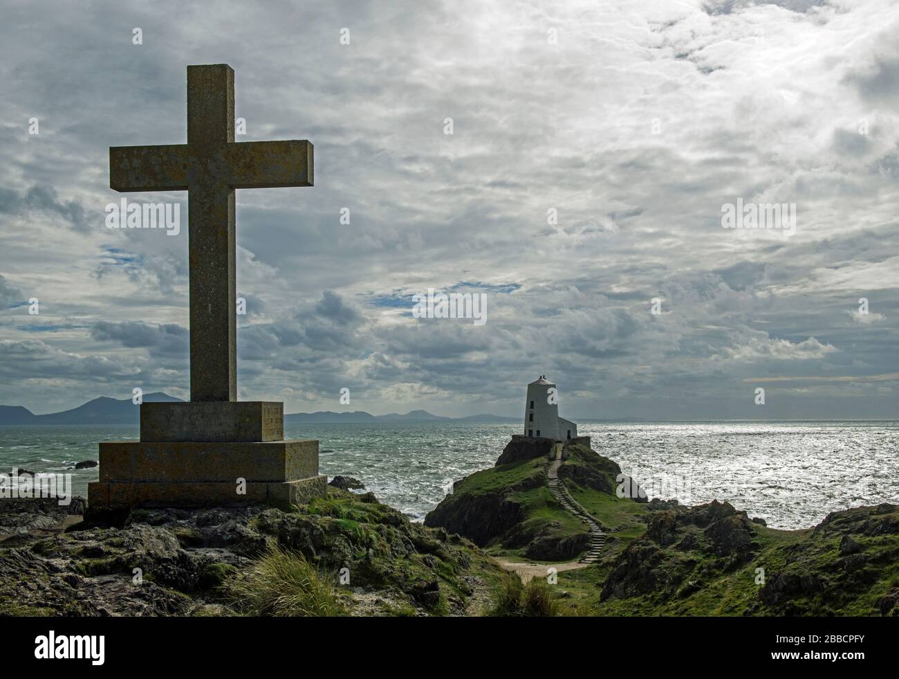 Llanddwyn Island vor der Küste von Anglesey. Dies zeigt einen der mehreren Kreuze auf der Insel zusammen mit dem Leuchtturm Ty Mawr mit silberfarbenem Sonnenuntergang Stockfoto