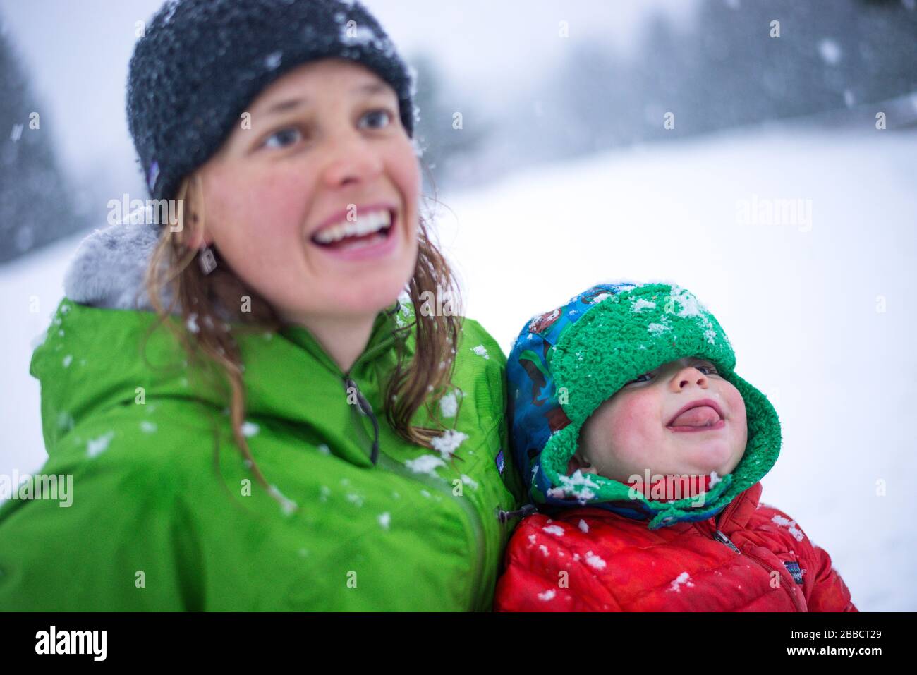 Mutter und junge Sonne, die im Winter in British Columbia mit Schneeflocken spielen Stockfoto