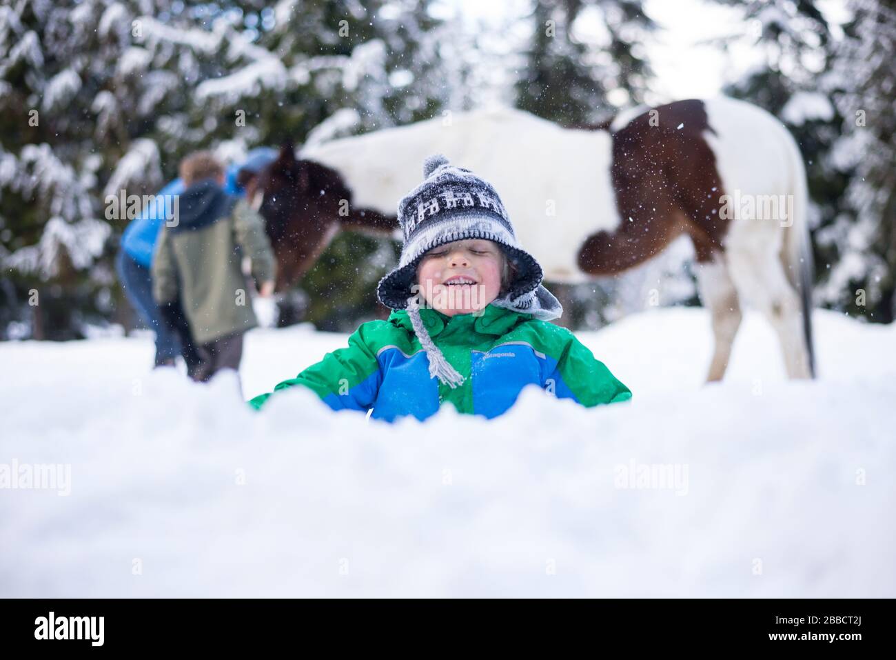 Ein kleiner Junge, der im Schnee vor einem Pferd in British Columbia spielt Stockfoto