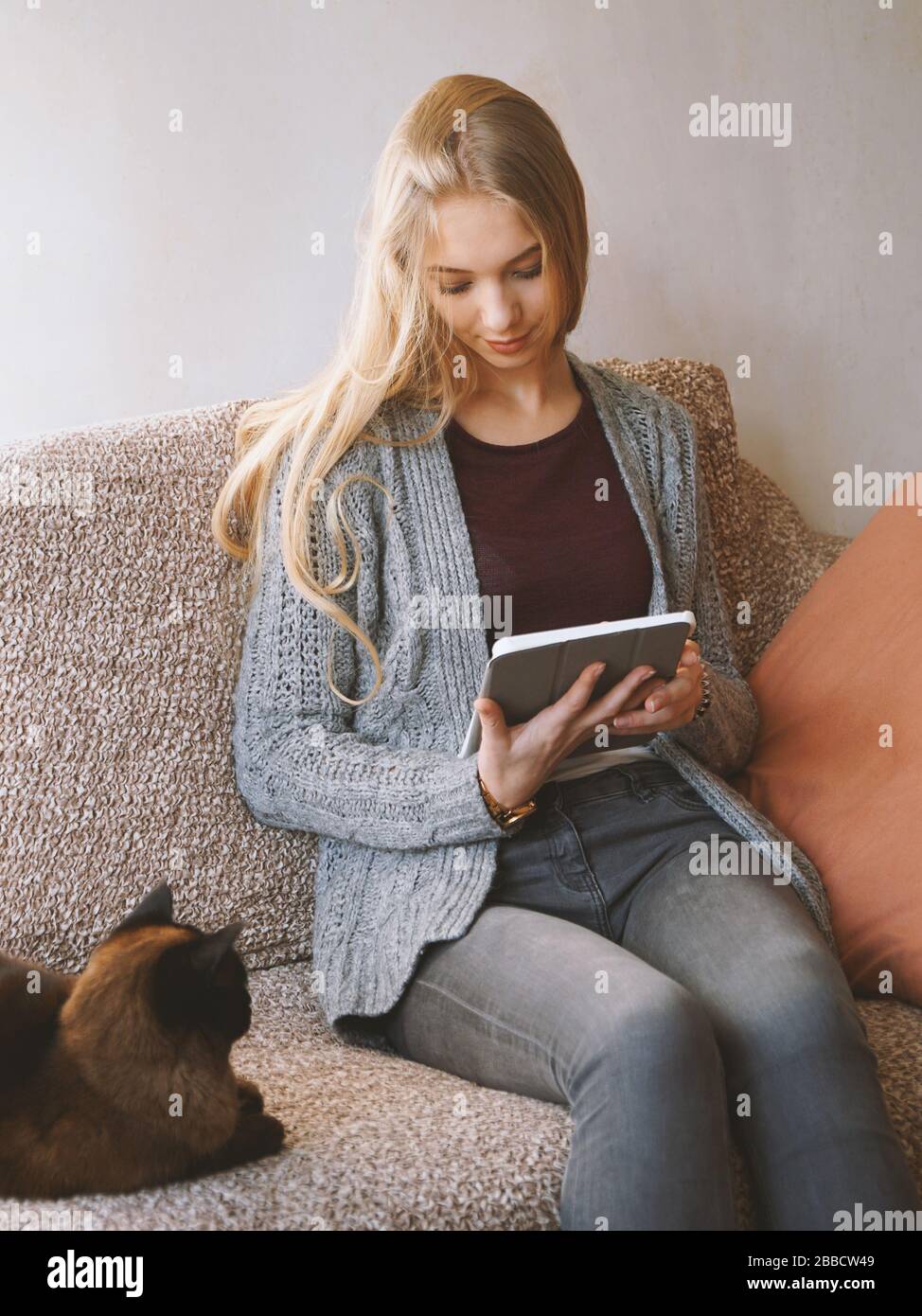 Bleiben Sie zu Hause Teenager-Mädchen Lesen Sie E-Book oder verwenden Sie einen Tablet-Computer, während Sie auf einem Sofa mit Katze sitzen - Online-Kommunikation während der Quarantäne Stockfoto