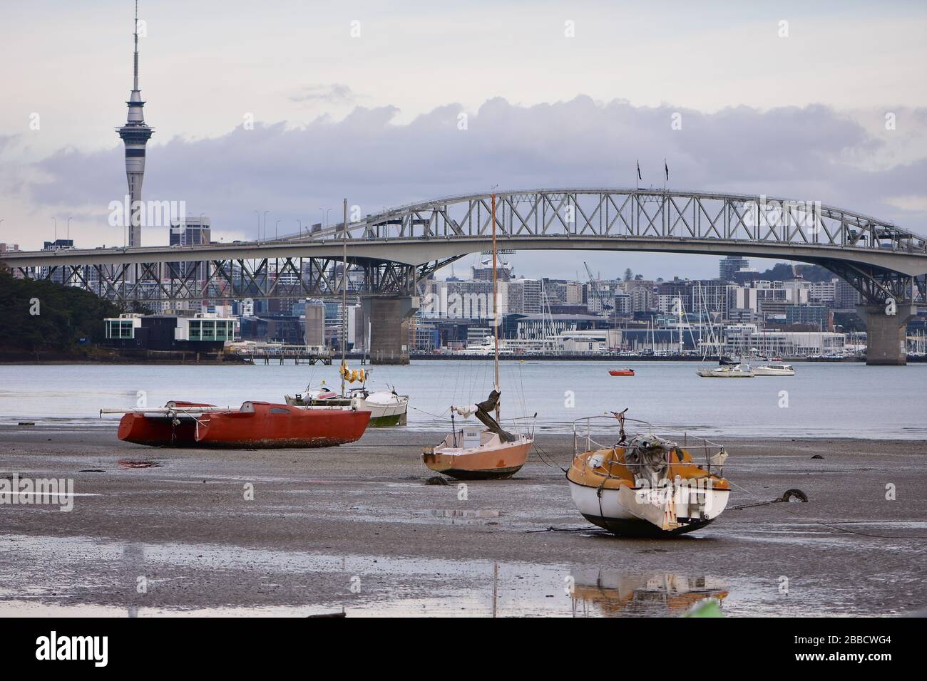 Segelboote, die bei Ebbe auf dem schlammigen Boden der Little Shoal Bay sitzen und im Hintergrund Blick auf Harbour Bridge und Auckland CBD haben. Stockfoto