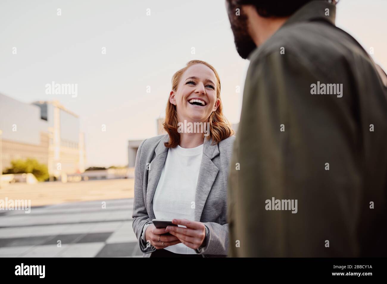 Porträt einer erfolgreichen und lachenden Geschäftsfrau im Gespräch mit männlichen Lebensgefährten auf der Straße der Stadt Stockfoto