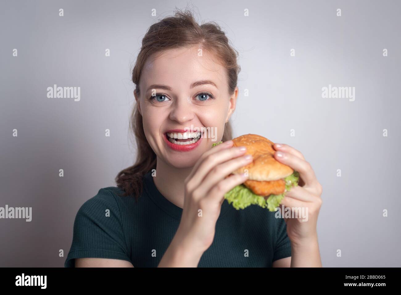 Lächelndes Mädchen der jungen kaukasischen Frau, das Hühnerburger isst Stockfoto