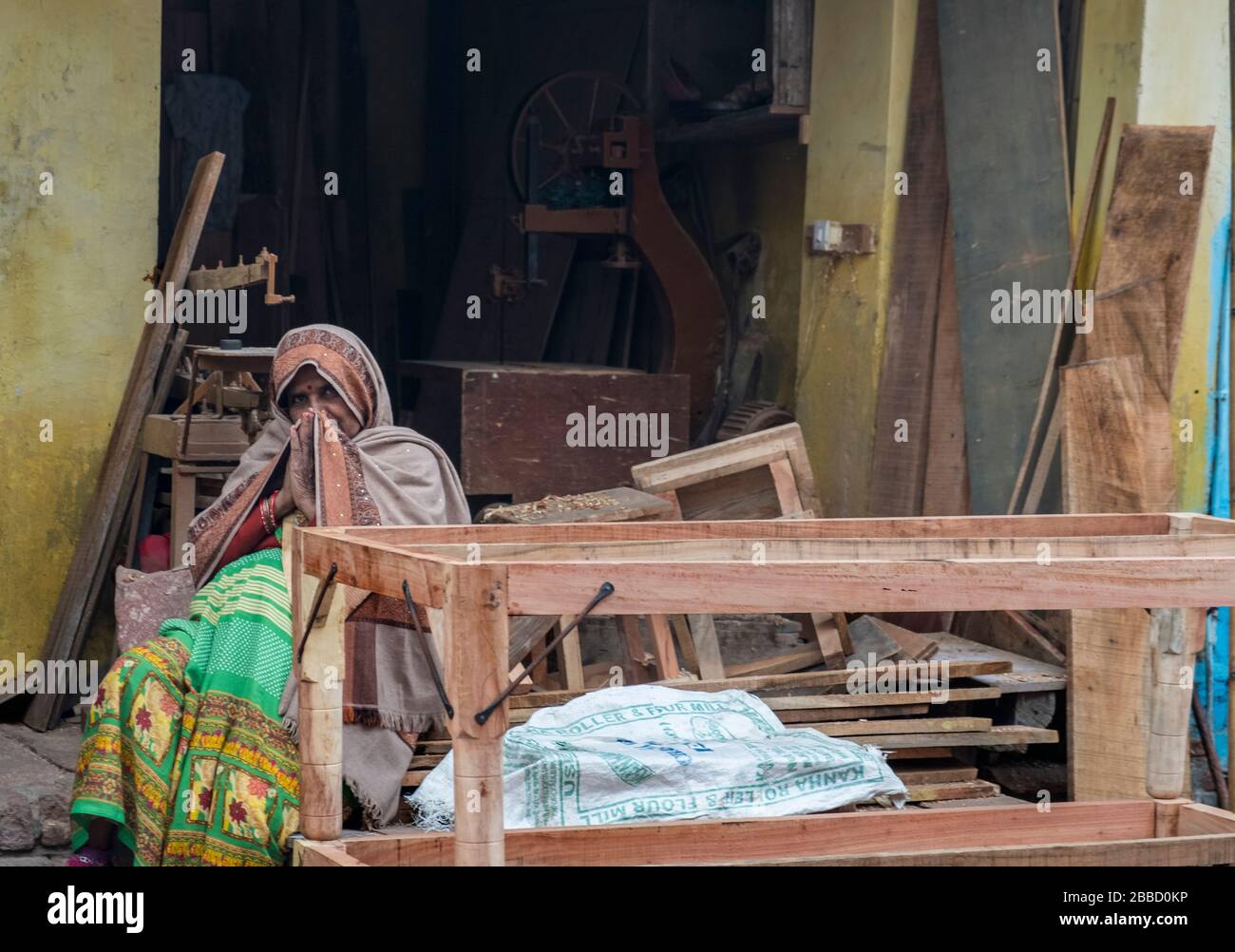 Alte indische Frau sitzt vor einer Familie Tisch Herstellung Werkstatt, Begrüßung Passanten vorbei Stockfoto