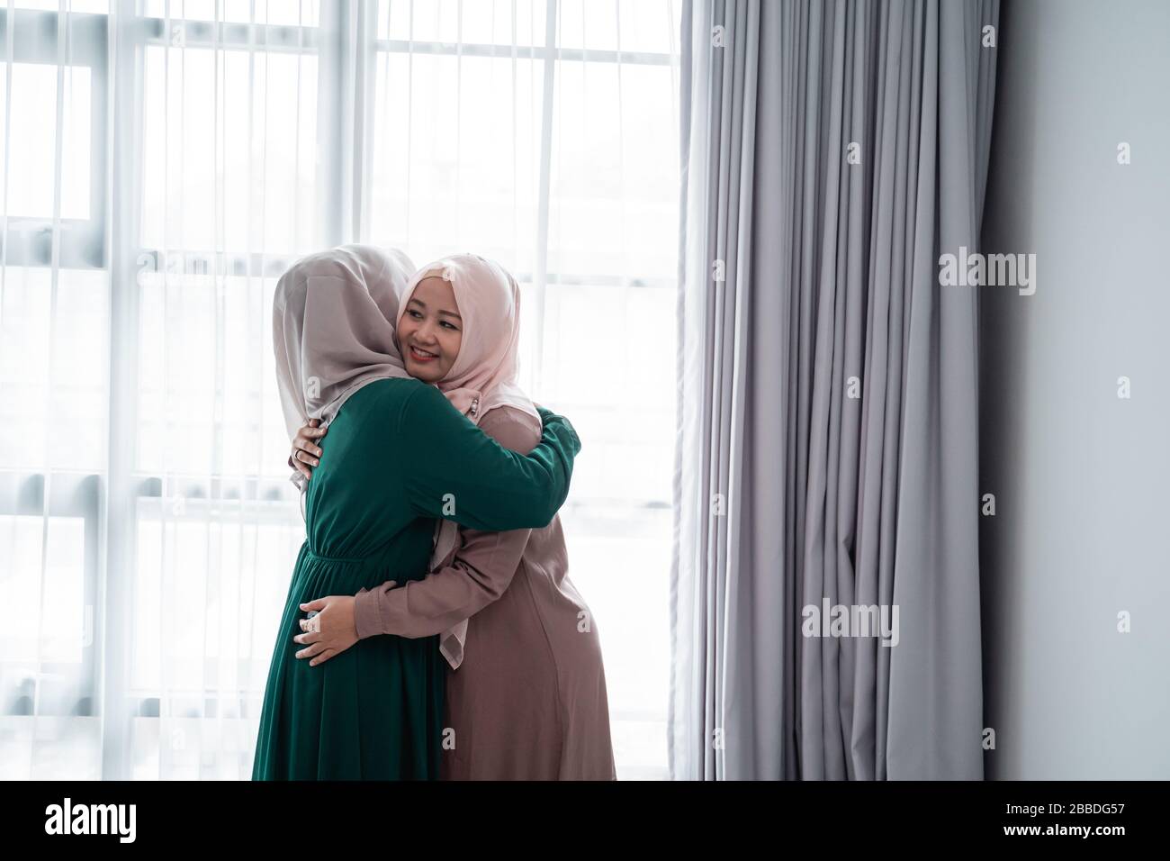muslimische Hijab-Frau, die glücklich nach Hause entregt, öffnet die Tür trifft sich und umarmt ihre Schwester Stockfoto