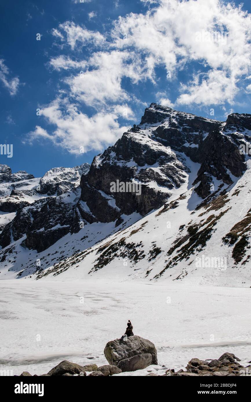 Foto eines verschneiten Berggipfels, der Mann sitzt mit dem Rücken zur Kamera und macht selfie Stockfoto