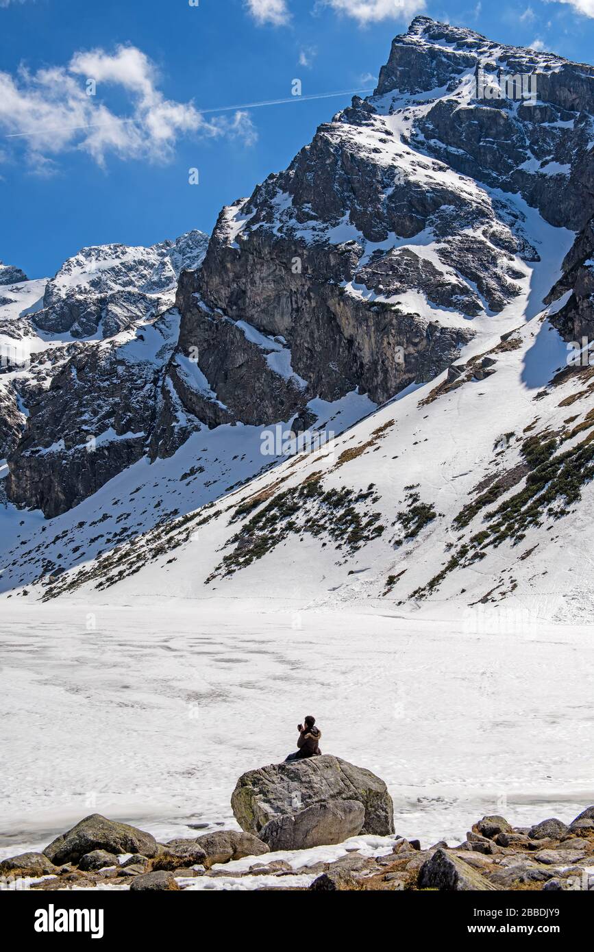 Foto eines verschneiten Berggipfels, der Mann sitzt mit dem Rücken zur Kamera und macht selfie Stockfoto