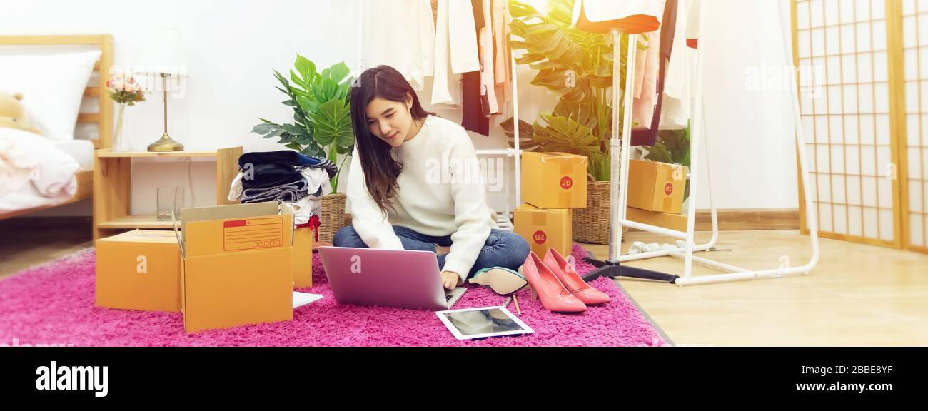 Arbeiten Sie von zu Hause aus. Glückliche Frauen, die Produkte online verkaufen, beginnen Sie mit einem Laptop auf Holzboden mit Modebekleidung Stockfoto