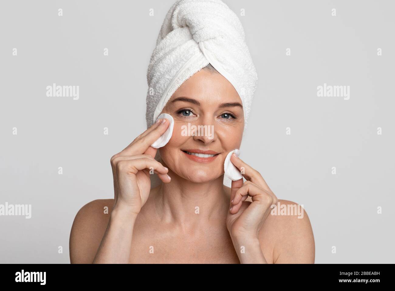 Schöne Frau mittleren Alters, die ihr Gesicht mit Toner und Baumwollpolstern säubert Stockfoto