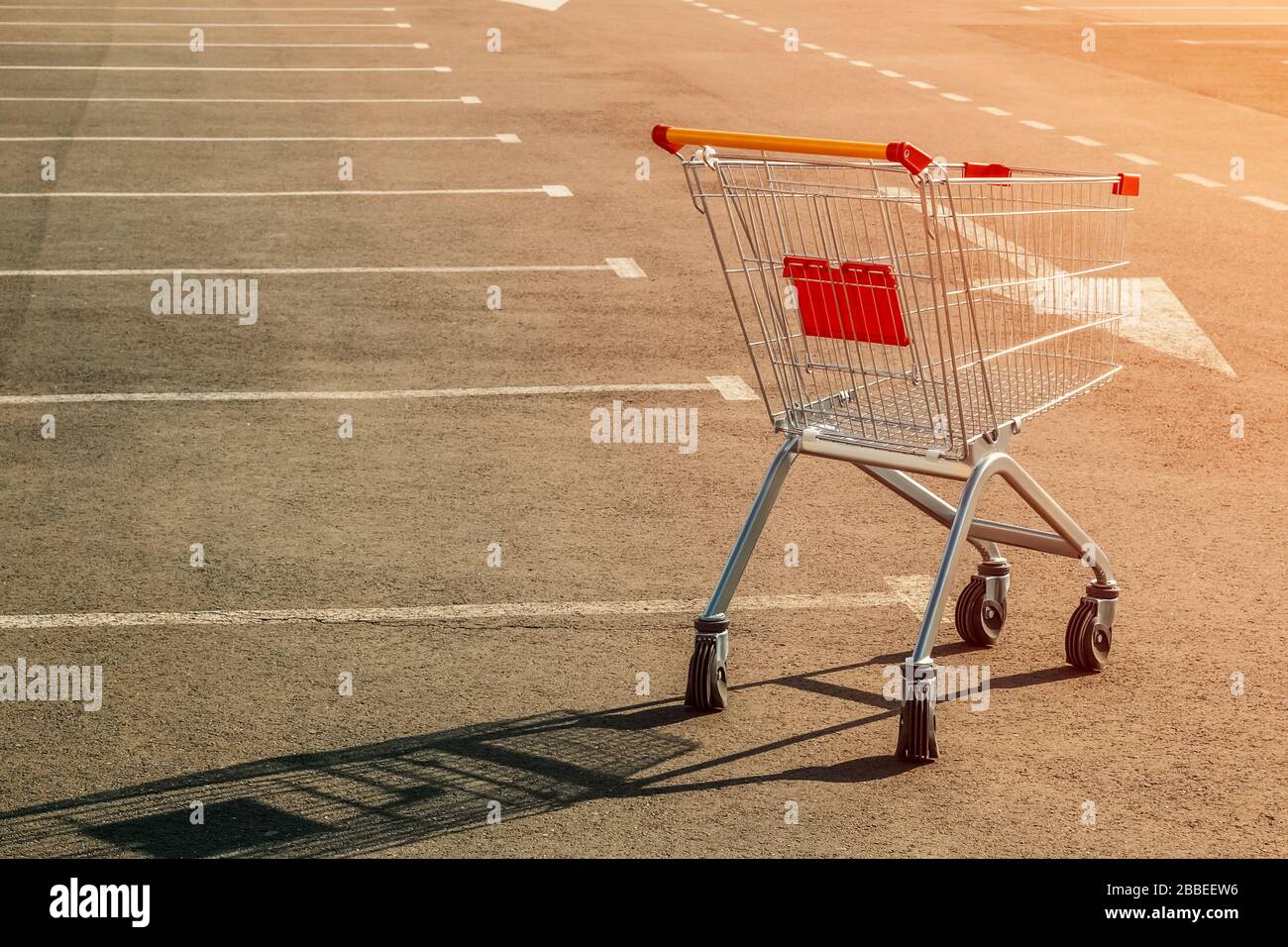 Einsamer leerer Lebensmittelwagen auf einem leeren Parkplatz in der Nähe eines Supermarktes bei Sonnenuntergang. Das Konzept der Lebensmittelknappheit, des Defizits, des Mangels an Menschen, der Quarantäne Stockfoto