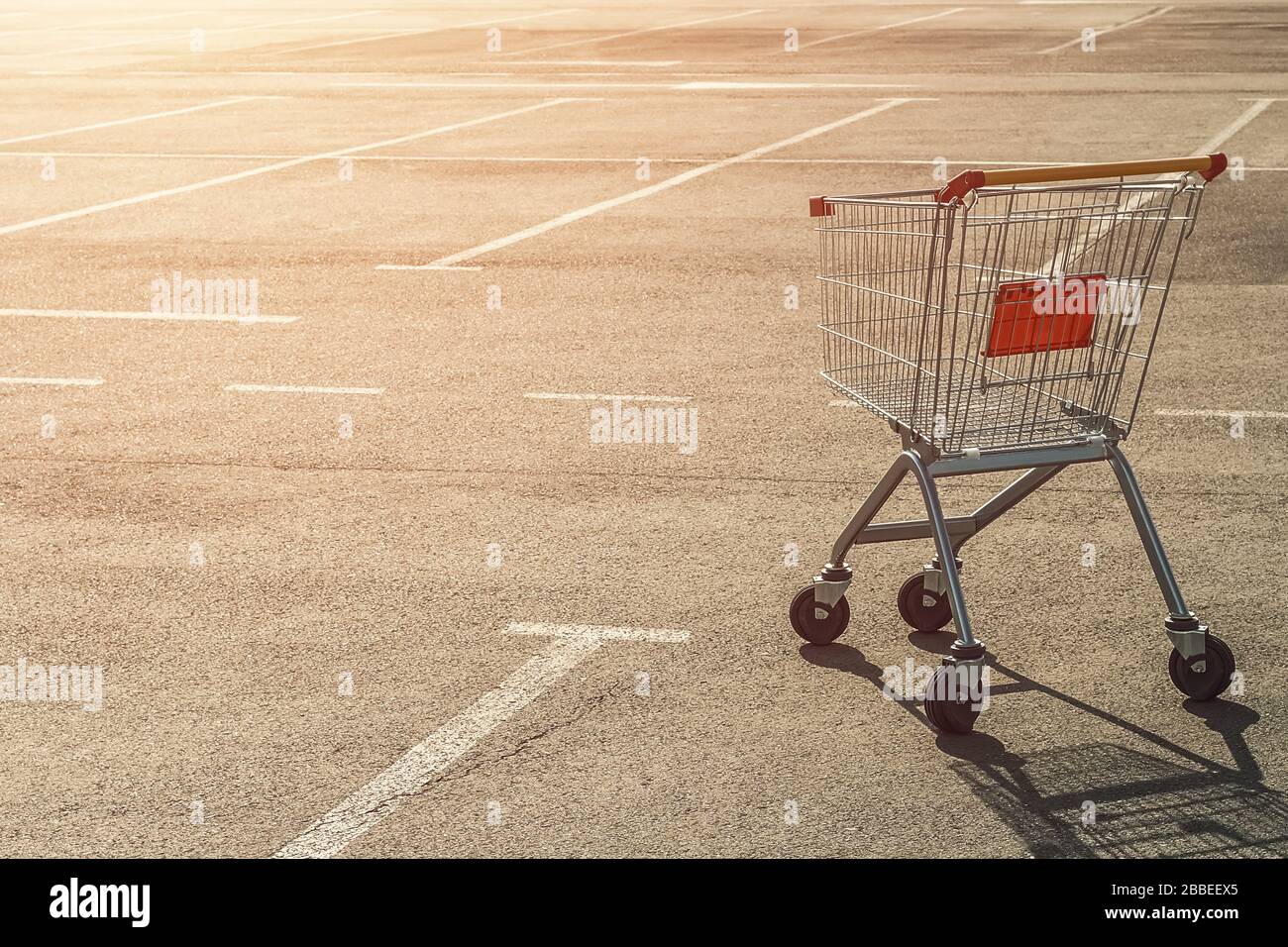 Leerer Einkaufswagen auf einem leeren Parkplatz in der Nähe eines Supermarktes, ohne Menschen bei Sonnenuntergang. Stockfoto