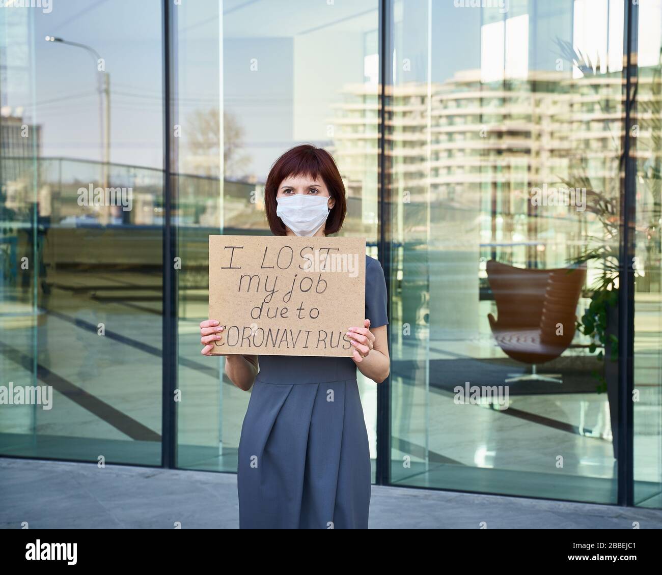 Frau in Maske hält Zeichen "Ich habe meinen Job wegen Coronavirus verloren" Konzept des Arbeitsplatzverlustes aufgrund der COVID-19-Virus-Pandemie. Weiblich steht vor Hintergrund o Stockfoto