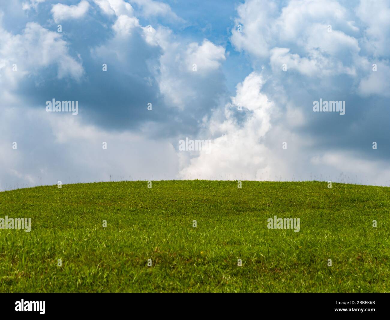 Landschaft mit grünem Gras auf einem kleinen Hügel und blauem Himmel mit Wolken Stockfoto