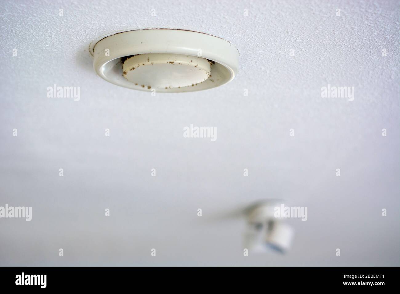 Verschmutztes altes gelbes Ventil für die Deckenbelüftung, das mit Staub und Schimmel bedeckt ist. Helle Flecken im Hintergrund Stockfoto