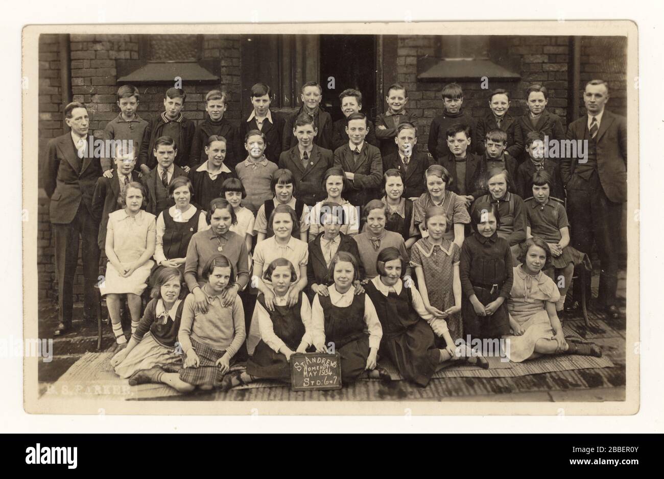 Postkarte junger Kinder (Standard 6 und 7) aus den frühen 1900er Jahren, die draußen für Fotos posieren, St. Andrew's School, Homer Street, Manchester, England, Großbritannien vom Mai 1934 Stockfoto