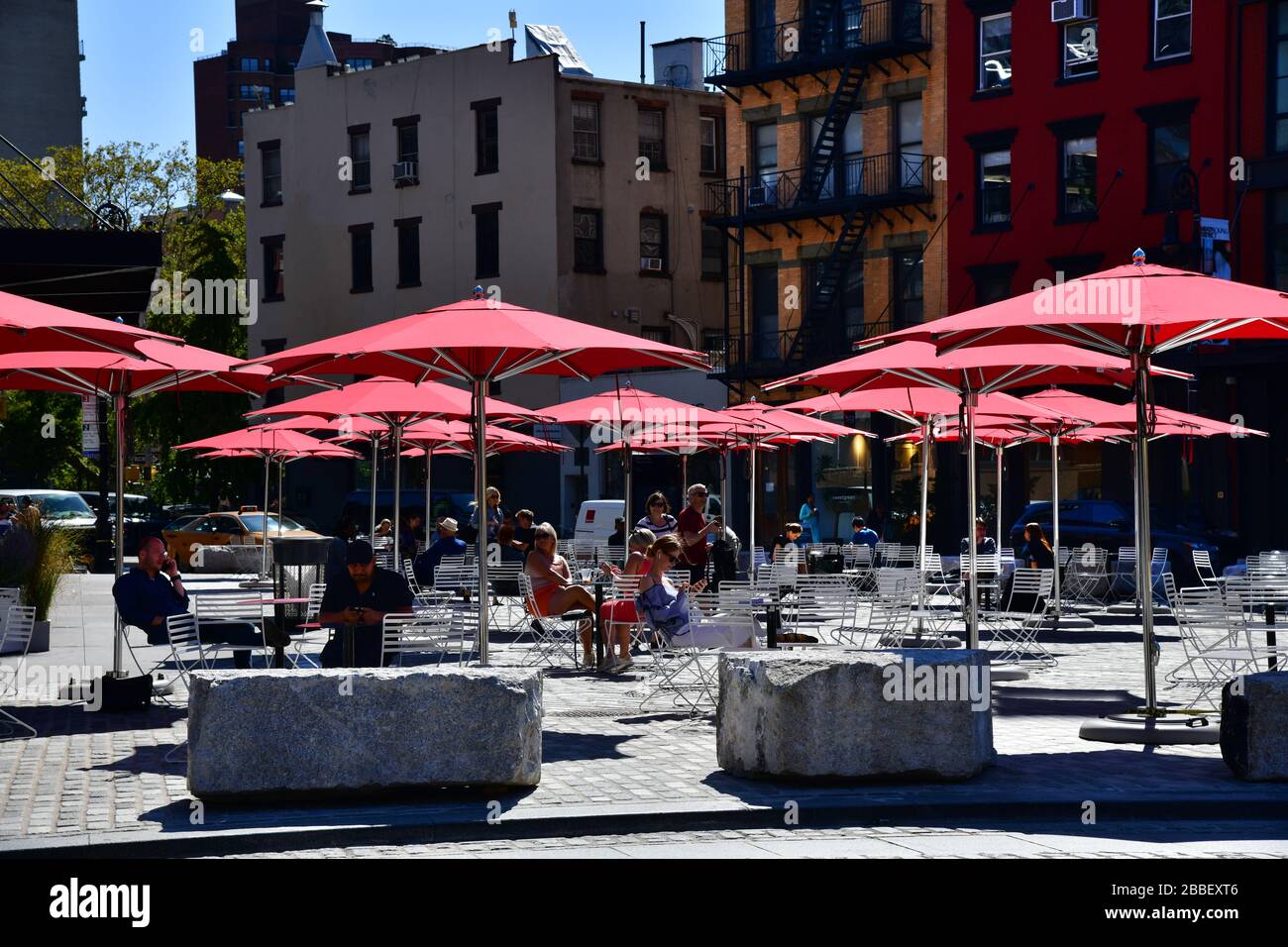 New York, USA: Blick auf den Platz mit roten Sonnenschirmen an der Kreuzung von 9th Av und 14th Street; Menschen in der Sonne entspannen Stockfoto