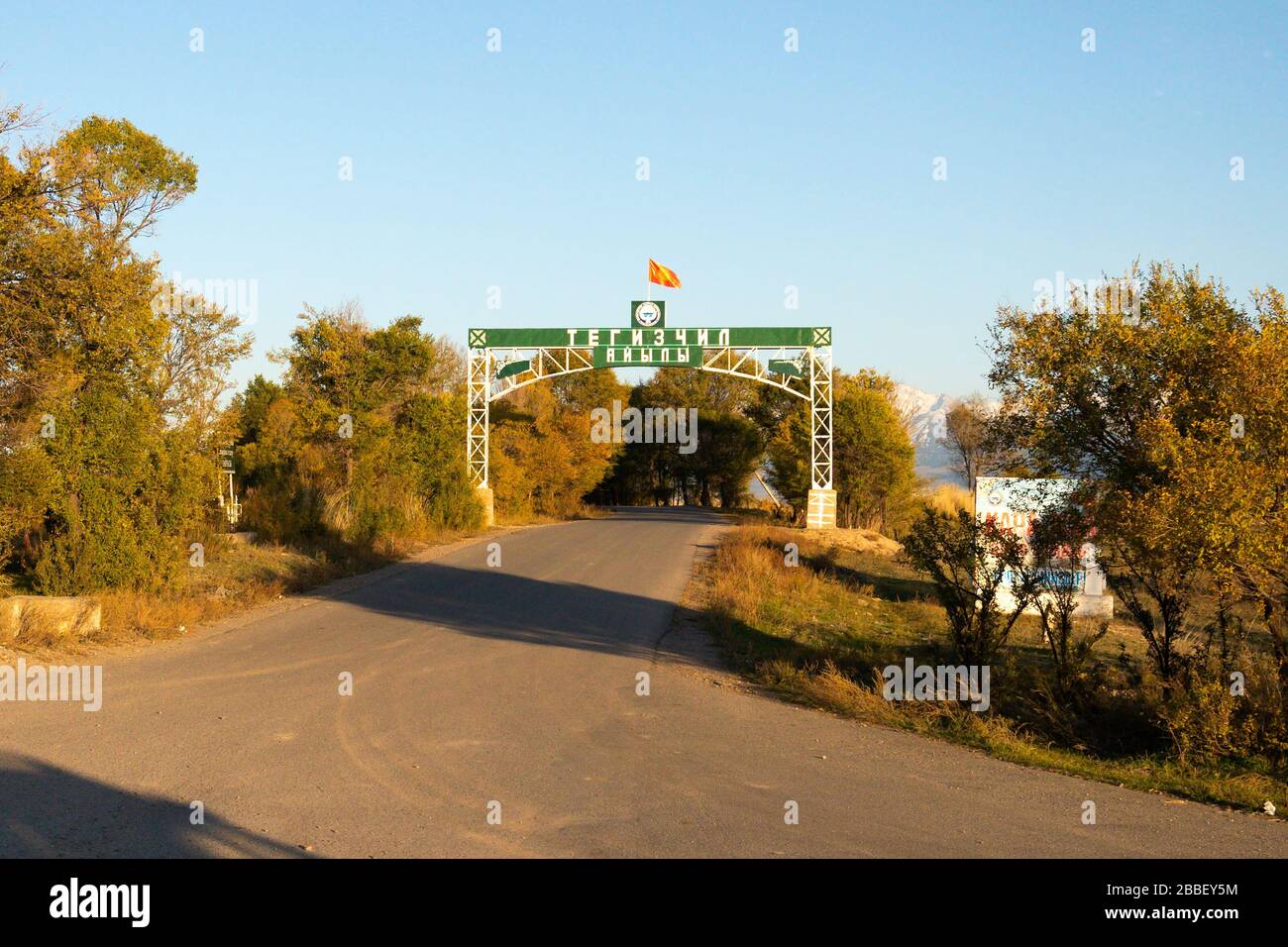 Blick auf die Bäume in einem Park mit einem Portikus, der die kirgisische Flagge und das kyrillische Alphabet zeigt. Stockfoto