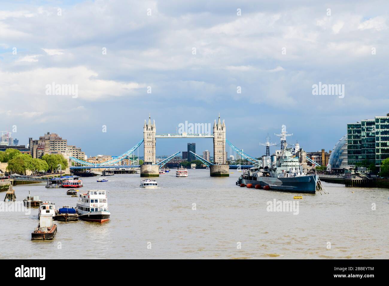 Die Tower Bridge öffnet für ein Kreuzfahrtschiff in London, England. Die "HMS Belfast" befindet sich auf der rechten Seite. Stockfoto