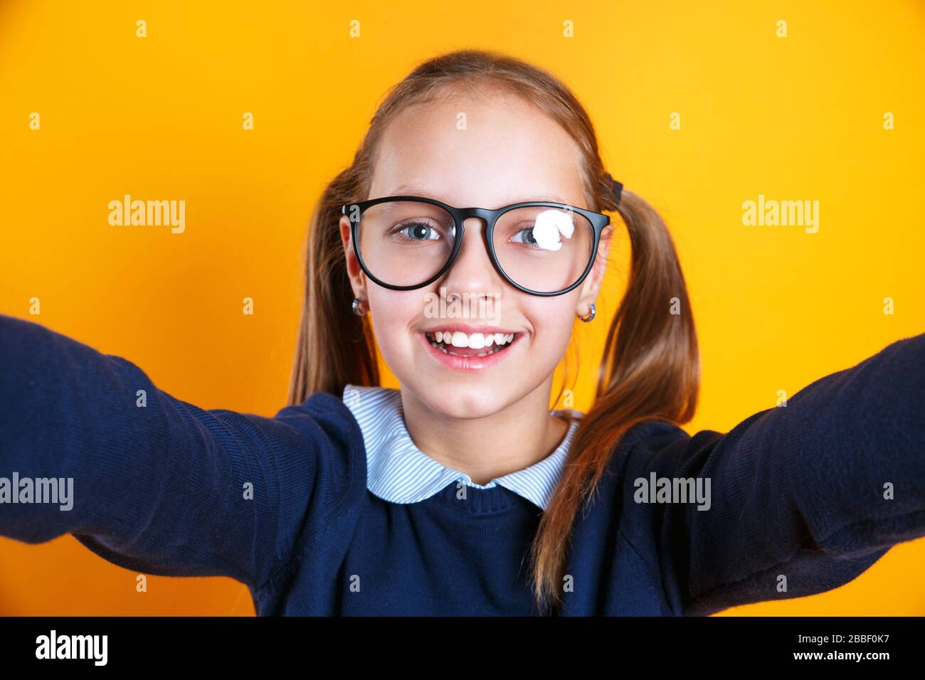 Nahaufnahme des kleinen 12-13-jährigen Mädchens in Brille, das selfie auf dem Handy auf gelbem Hintergrund macht. Stockfoto