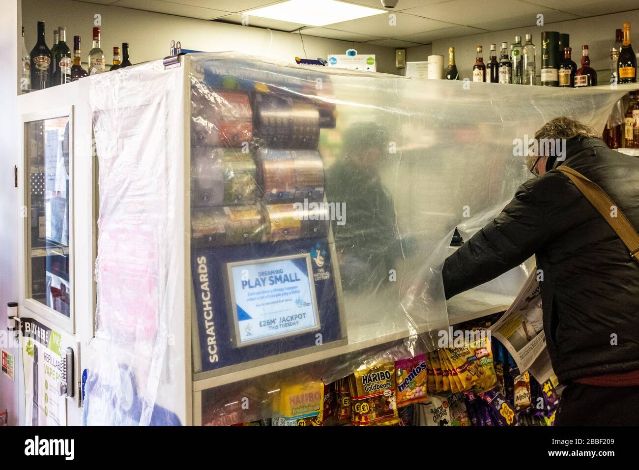 Ladenbesitzer im Zeitungskiosk und Convenience-Store in England, der Vorsichtsmaßnahmen bei der Pandemie von Coronavirus ergreift. Hitchin, Hertfordshire, März 2020 Stockfoto