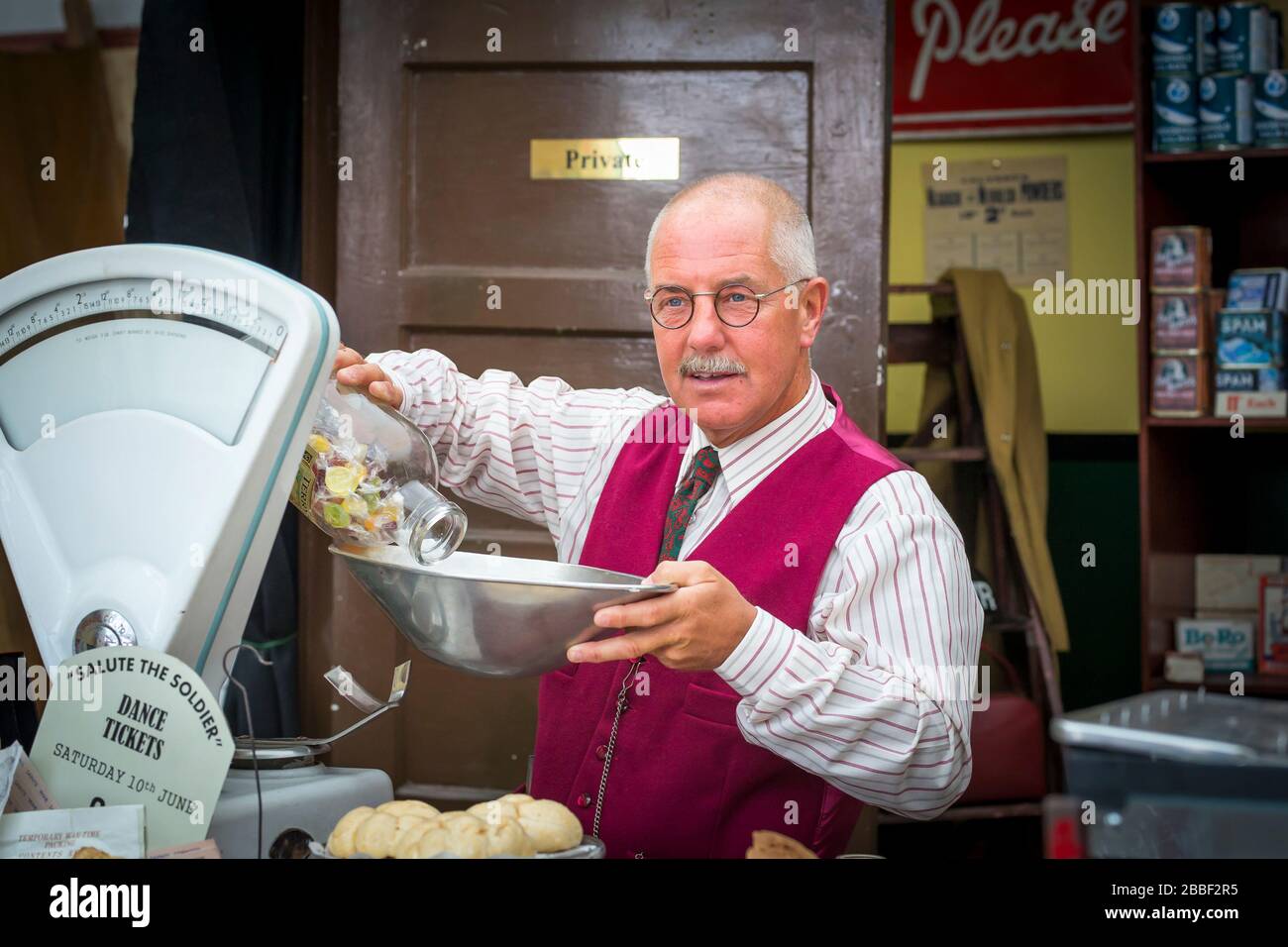 Isolierter Mann als Vintage-Lebensmittelgeschäft, Kriegsgeschäft, 1940er-WWII-Ereignis, Großbritannien. Altmodische WW2 Rationierung von Lebensmitteln: Wiegen von Süßigkeiten. Stockfoto