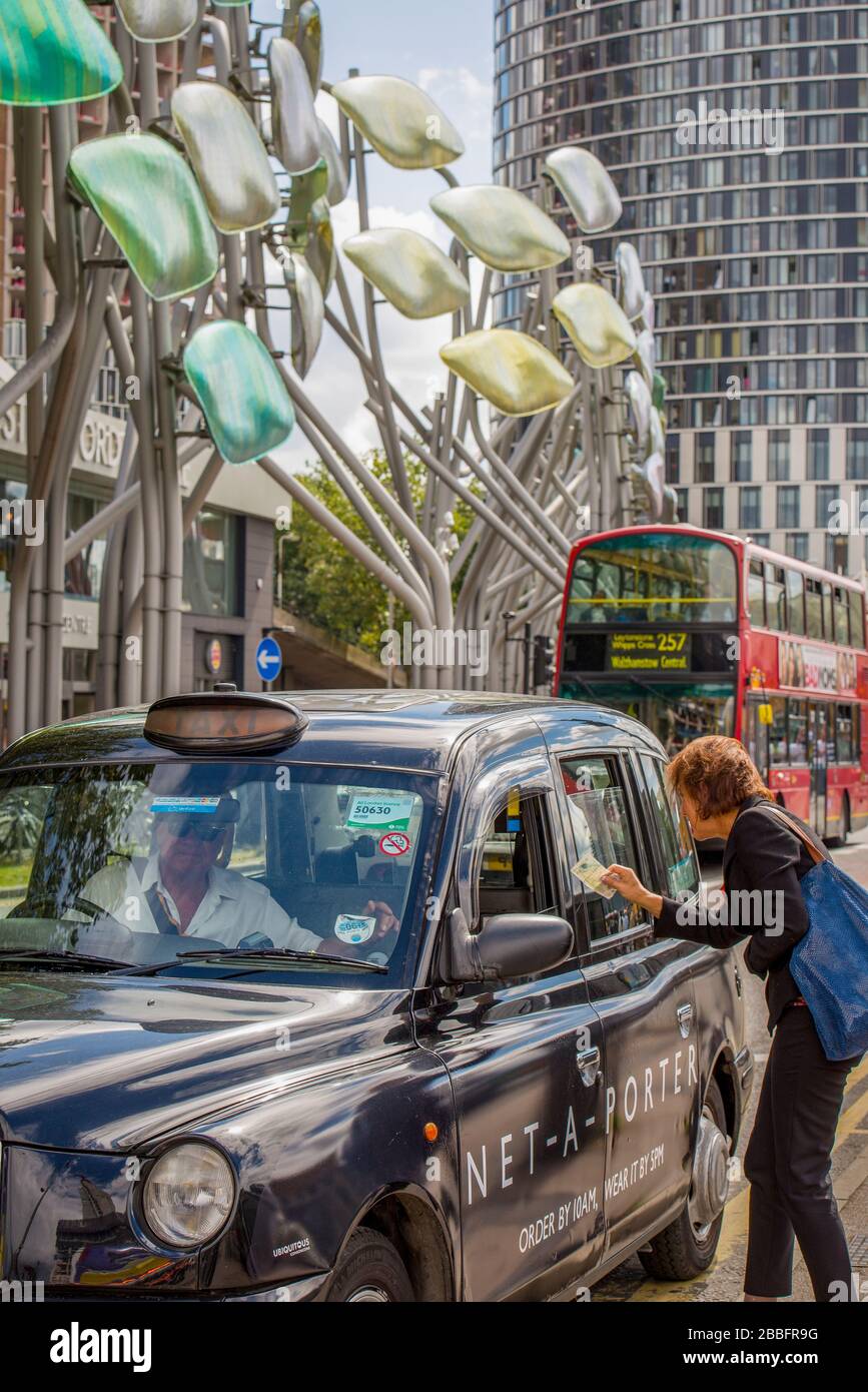 Eine Frau bezahlt bar an einen schwarzen Londoner Taxifahrer für ihre Fahrt zum Stratford Shopping Center in East London Stockfoto