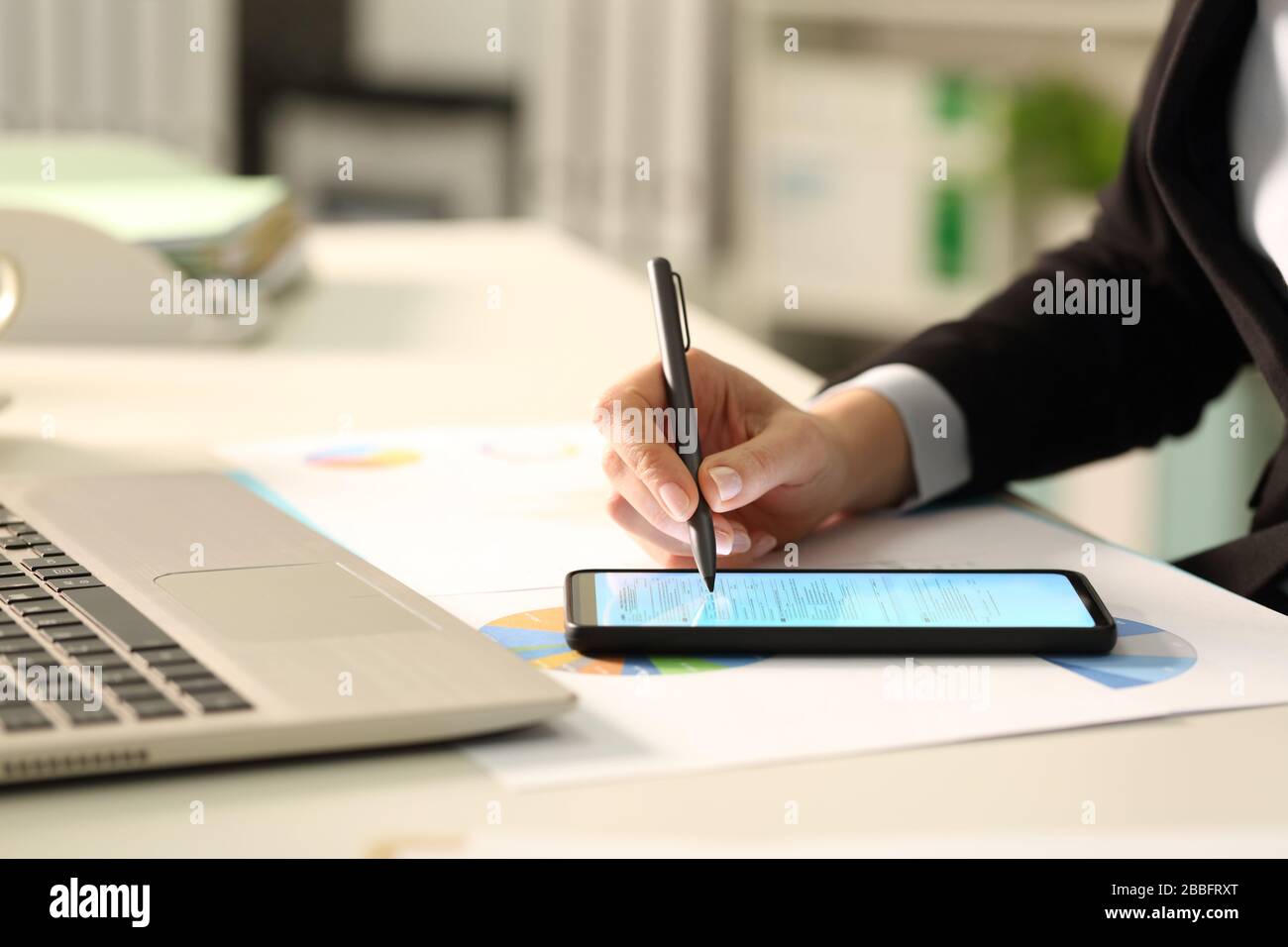 Nahaufnahme der Führungskraft Hände Ausfüllen des Dokuments mit einem Stift auf dem Smartphone auf einem Schreibtisch im Büro Stockfoto