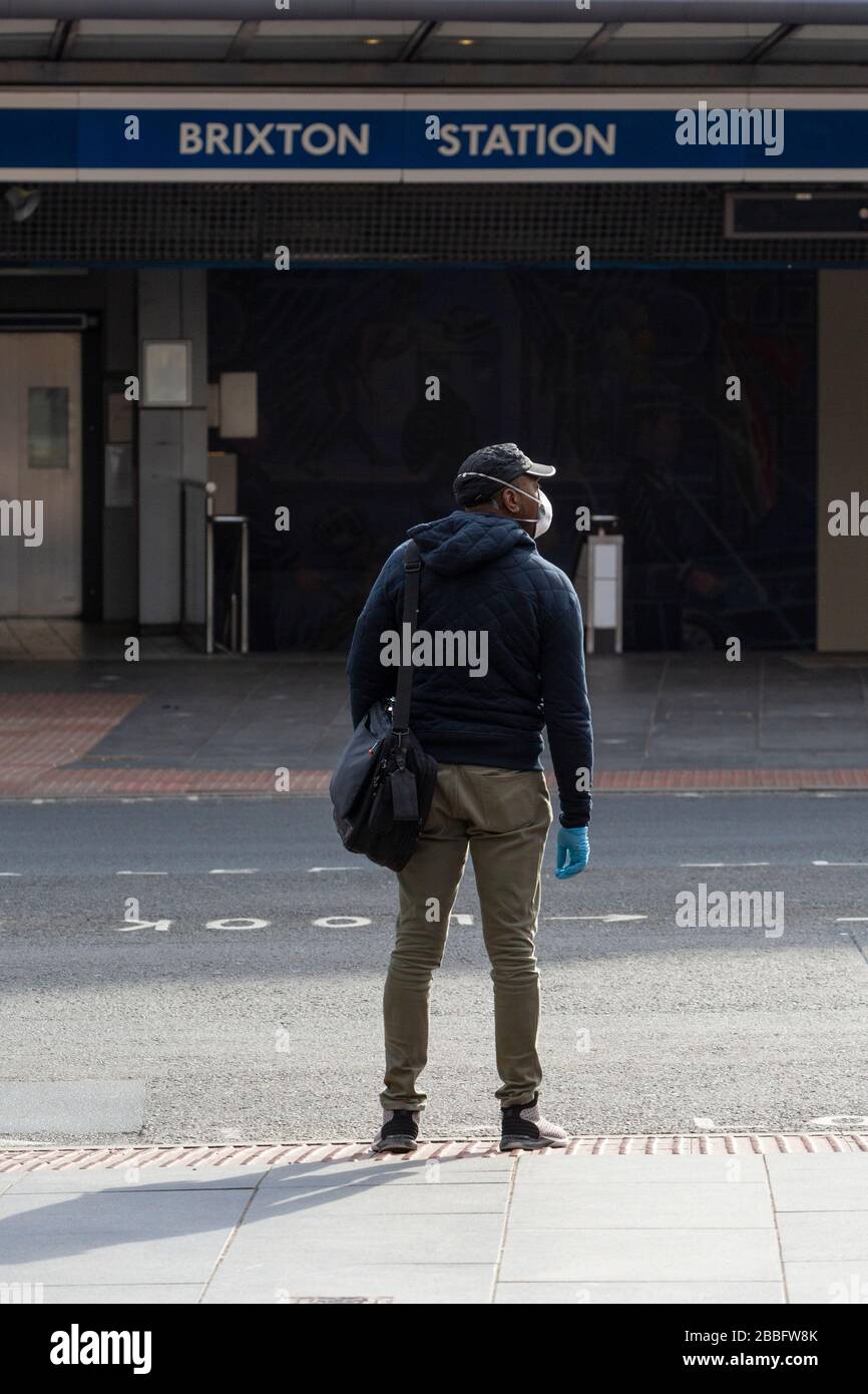 Mann mit Gesichtsschutzmaske und Handschuhen außerhalb der Brixton Station, während der Londoner Sperre aufgrund der Ausbreitung von Covid-19. Am 31. März 2020 aufgenommen Stockfoto