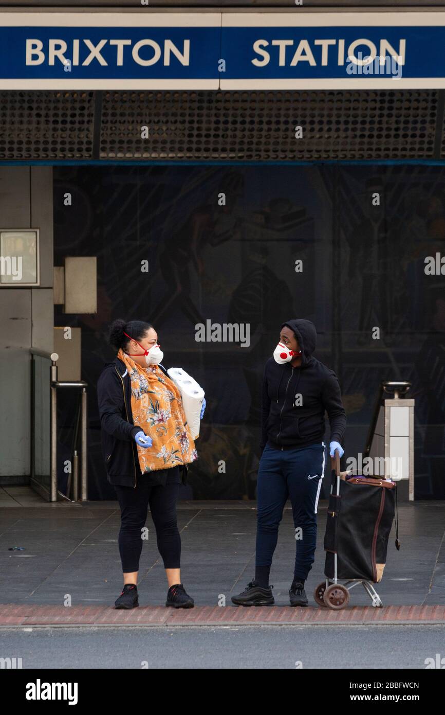 Ein Mann und eine Frau, die vor der Brixton Station stehende Gesichtsmasken und Handschuhe tragen, während der Londoner Sperre aufgrund der Ausbreitung von Covid-19. Genommen Stockfoto
