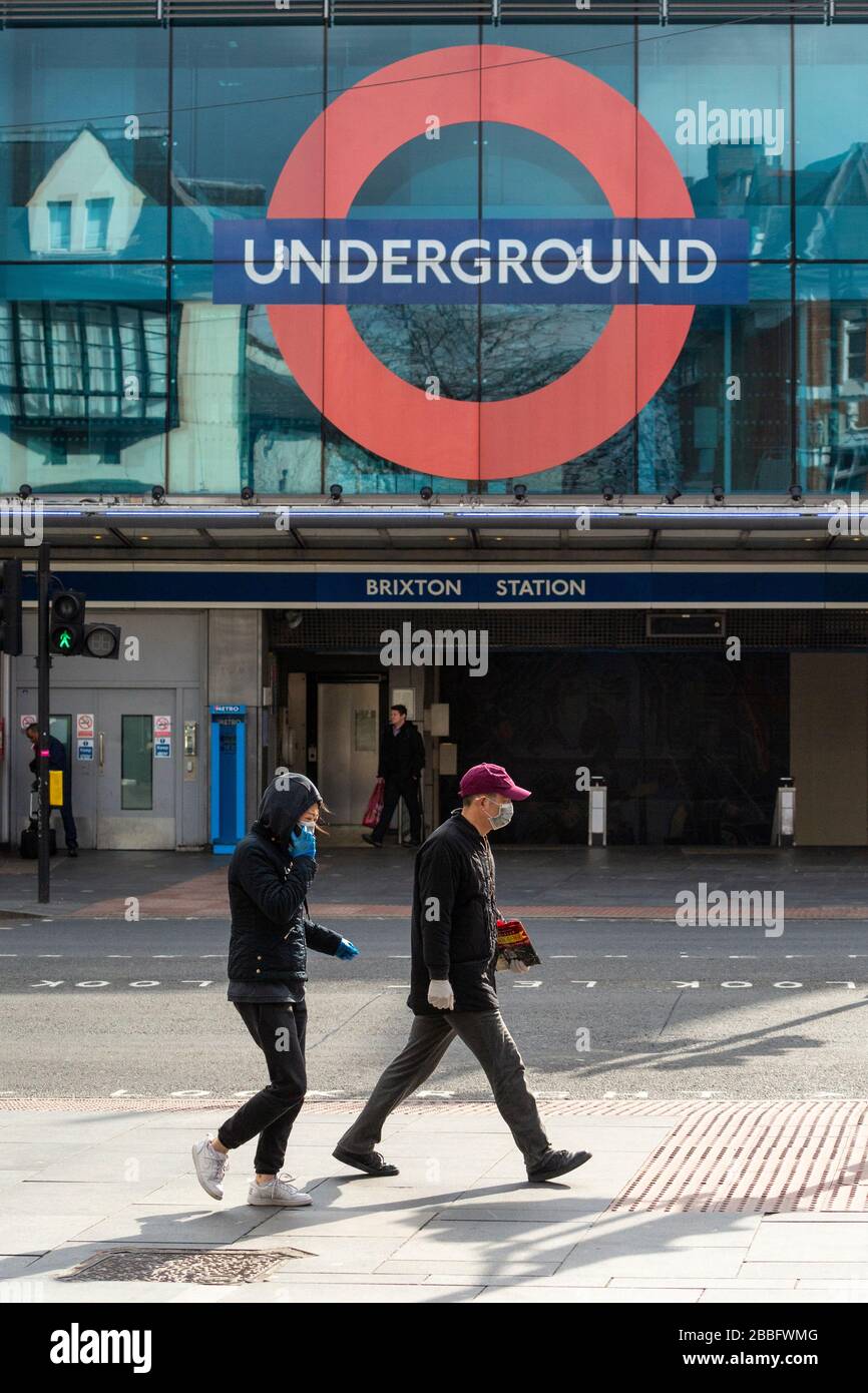 Zwei Personen mit Schutzausrüstung gehen an der Brixton Station vorbei, während der Londoner Sperrung aufgrund der Ausbreitung von Covid-19. Am 31. März 2020 aufgenommen Stockfoto