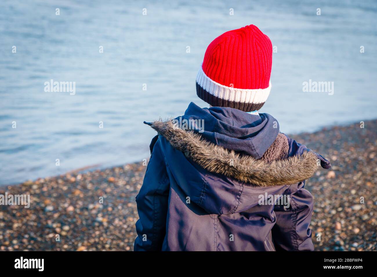 Junge wirft Steine ins Meer vom Strand Stockfoto
