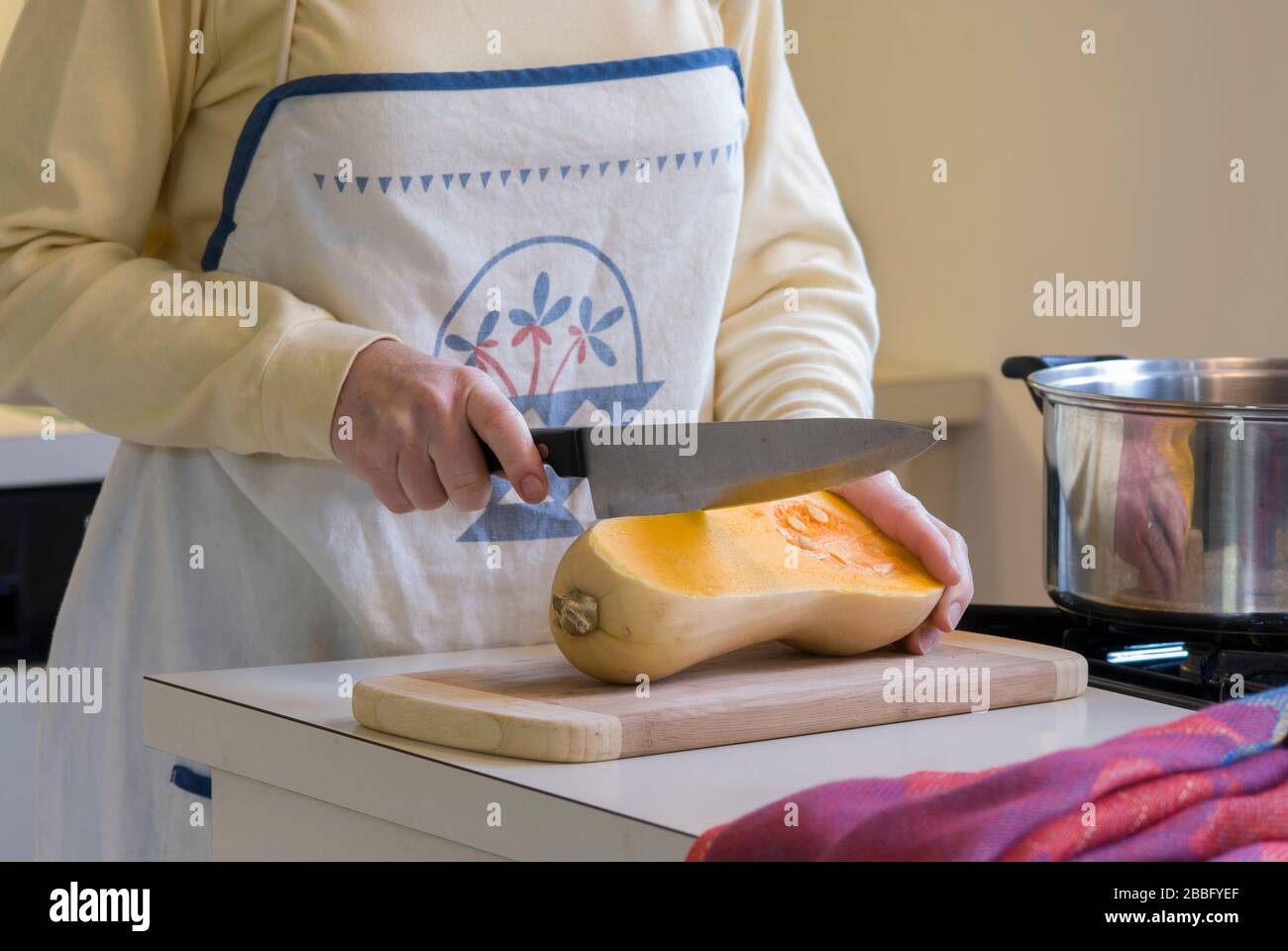 Frau in der Küche mit vier Kochfeldern zum Schneiden von Butternusskürbis zur Herstellung von Suppe Stockfoto