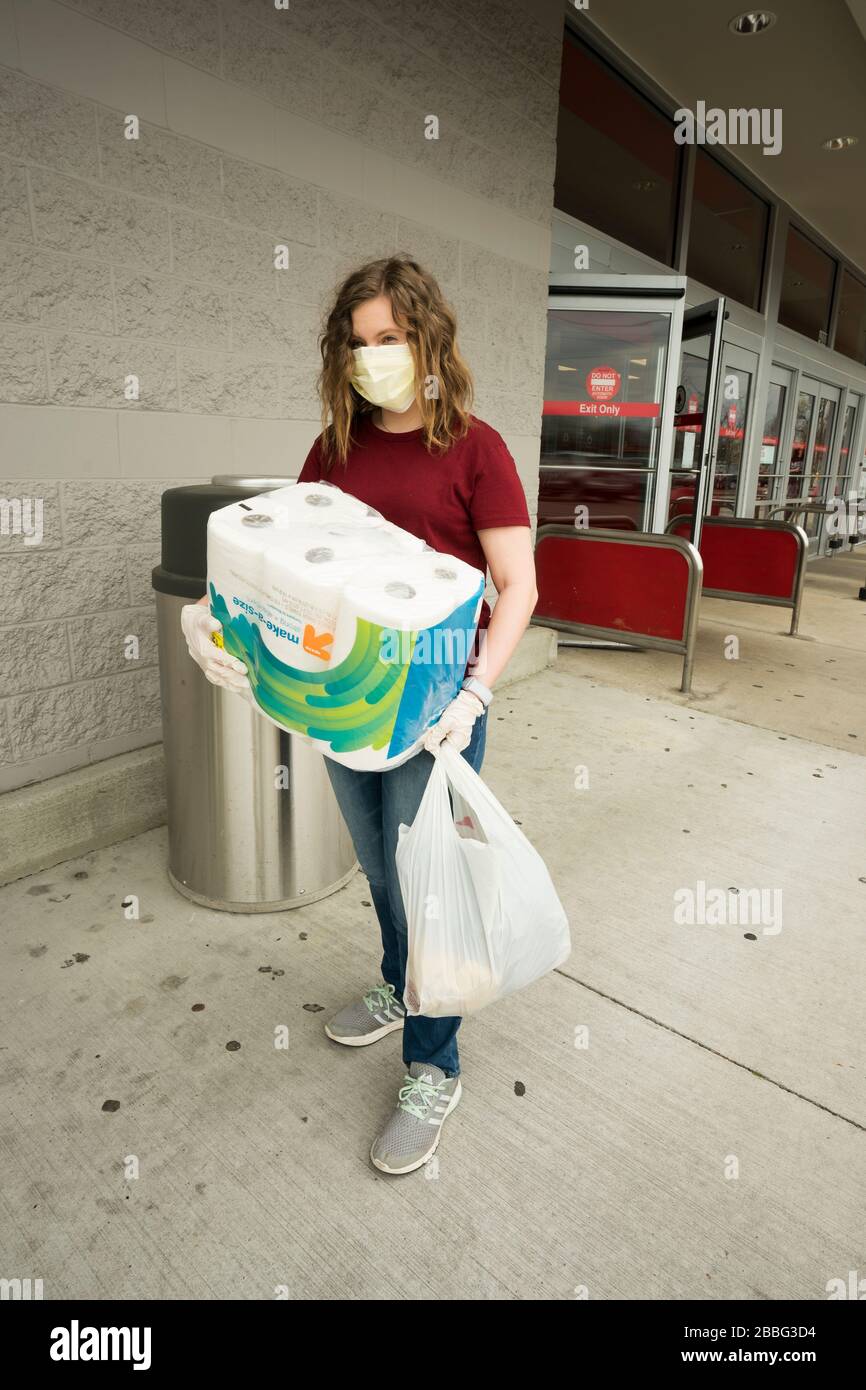 Indiana, USA - 24. März 2020: Eine blonde Frau, die eine Gesichtsmaske und Handschuhe trägt, verlässt einen Laden, in dem sie ein Paket mit Papiertüchern und anderen s gekauft hat Stockfoto
