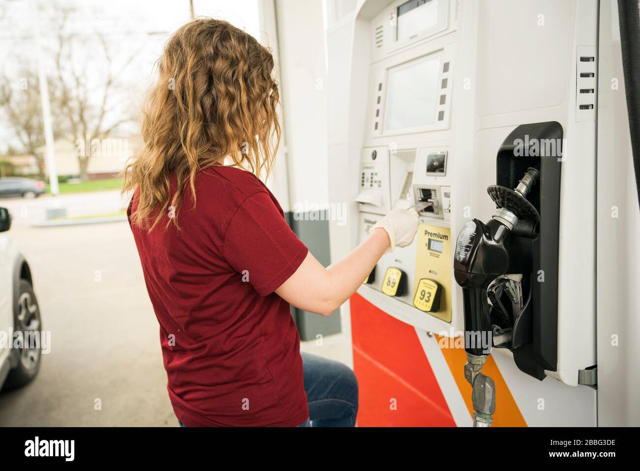 Indiana, USA - 24. März 2020: Eine blonde Frau, die Schutzhandschuhe trägt, füllt ihr Auto während des Corona-Virus COV mit Benzin an der Tankstelle Stockfoto