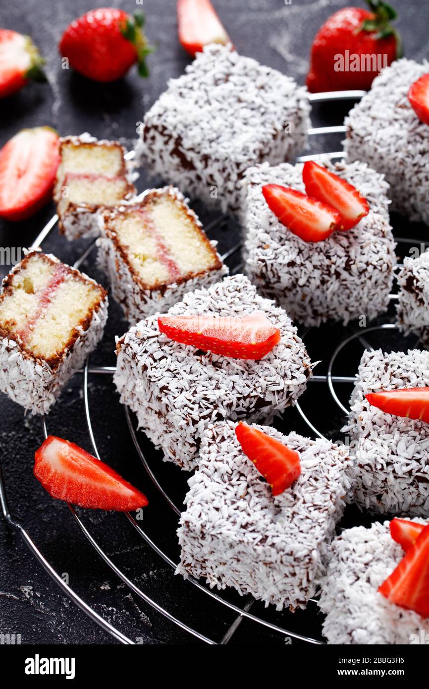 Lamington Kuchen ein australisches Dessert aus kleinen Würfeln oder Quadraten Biskuitkuchen, in Schokolade getaucht und dann mit frischen Erdbeeren in Kokosnuss gerollt Stockfoto