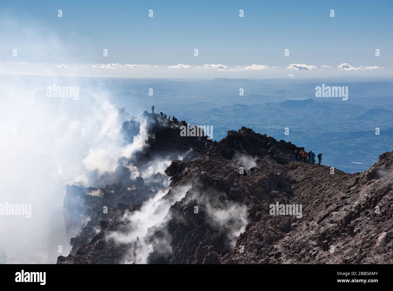 Wasserdampf und andere vulkanische Gase überlaufen die Gipfelkrater des Ätna und schütten sich über die oberen Hänge des Vulkans aus. Die Menschen verschwinden im Dampf. Stockfoto
