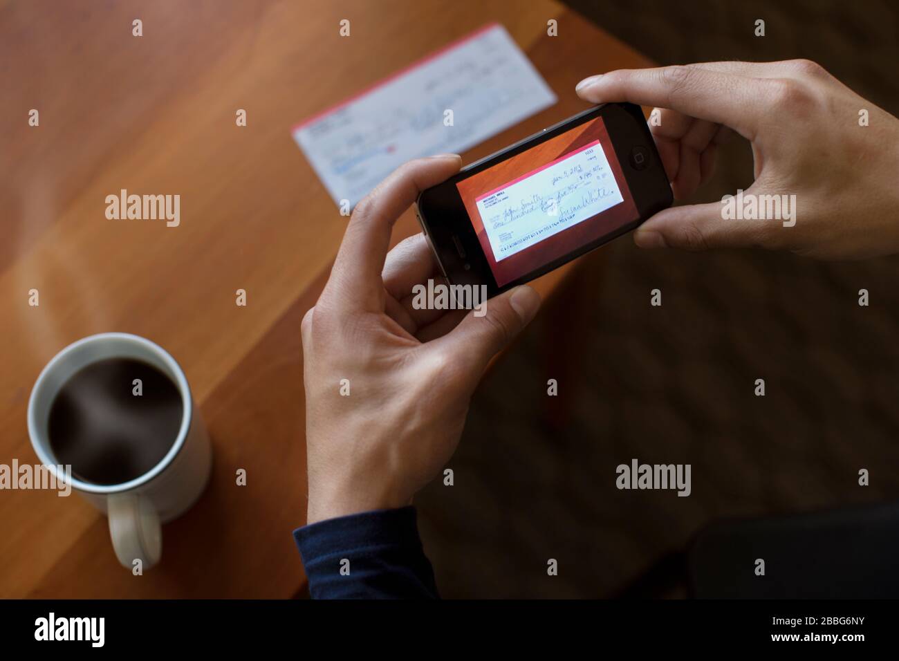 Hände eines jungen Mannes, der einen Scheck mit einem Smartphone fotografiert. Stockfoto