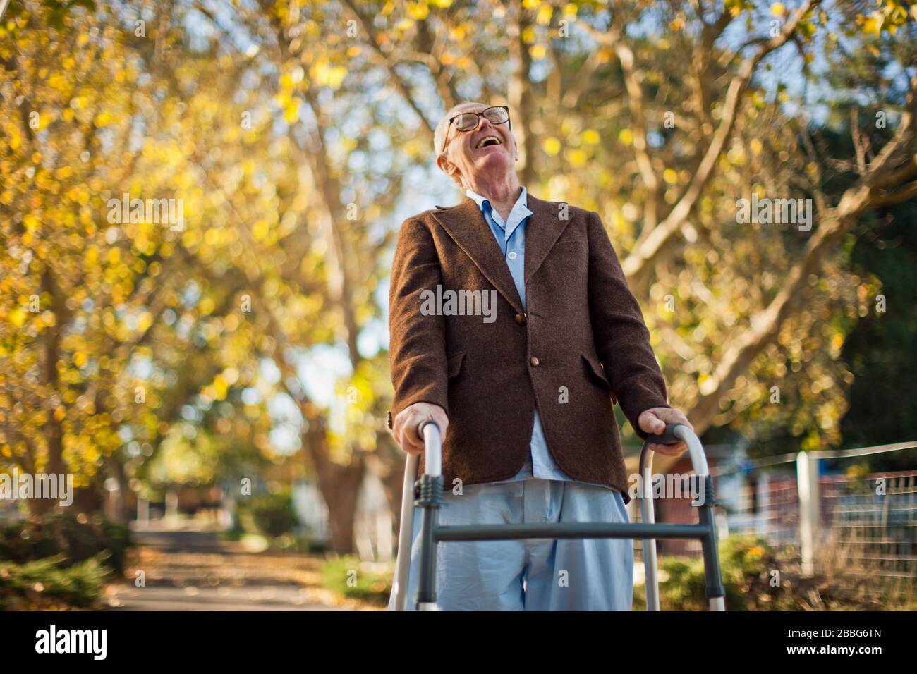 Lachender älterer Mann, der Spaß hat, durch einen Park mit einem Wanderrahmen zu gehen. Stockfoto