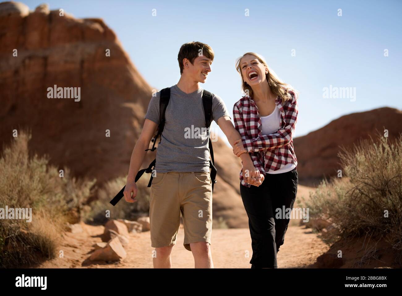 Lachende junge Frau, die sich mit ihrem Freund die Hände hält, während sie gemeinsam durch eine Wüste wandern Stockfoto