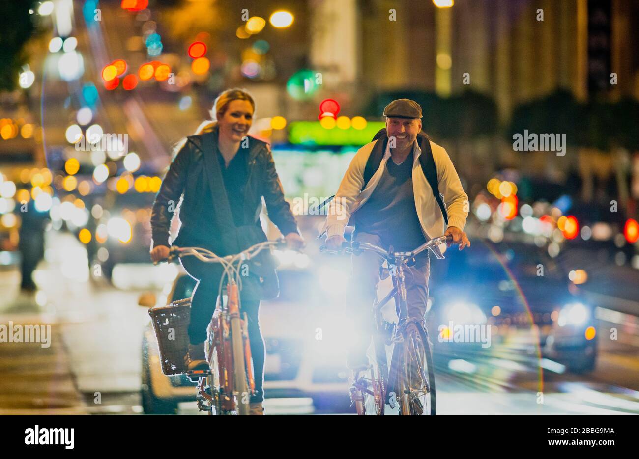 Reifer Mann und junge Frau fahren zusammen entlang einer belebten Straße in der Stadt bei Nacht Stockfoto