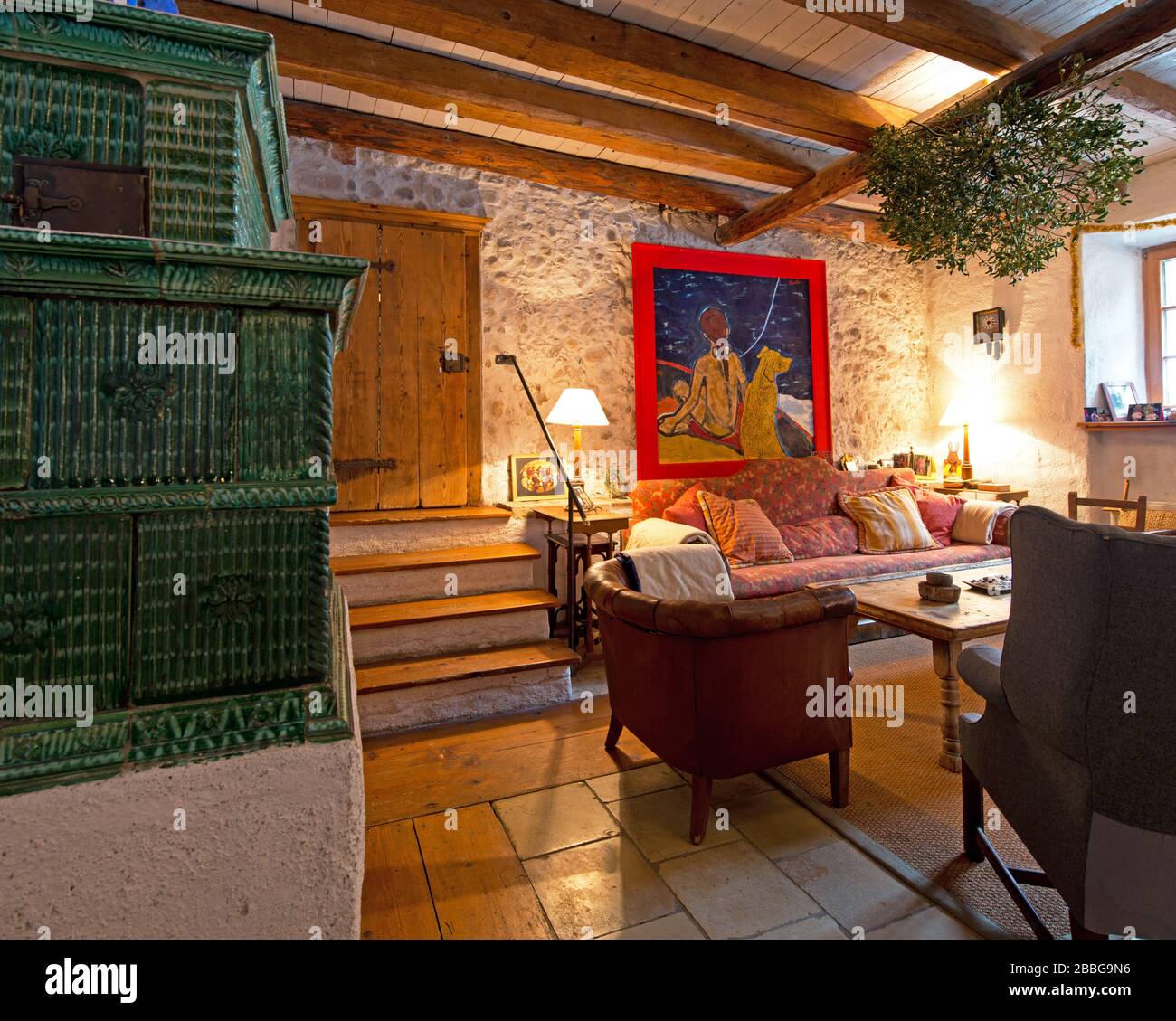 Wohnzimmer im Landhausstil mit grünem Kachelofen, Sofa, Holztramen und Ölgemälde Stockfoto