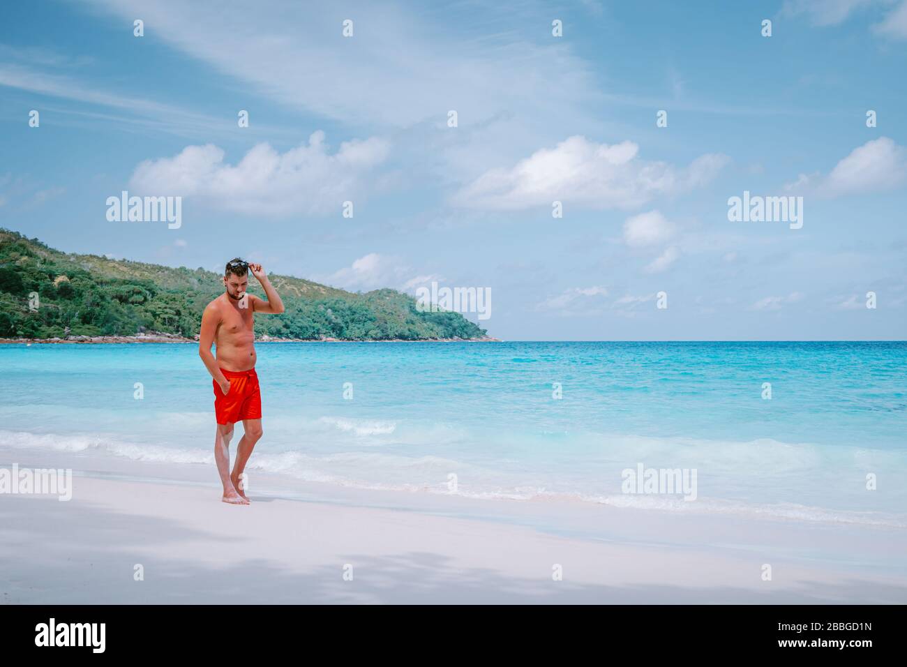 Cote D'Or Beach, Praslin Seychelles Tropical Island, junge Männer schwimmen kurz am weißen Strand mit riesigen Felsbrocken und Felsen und einem weißen tropischen Stockfoto