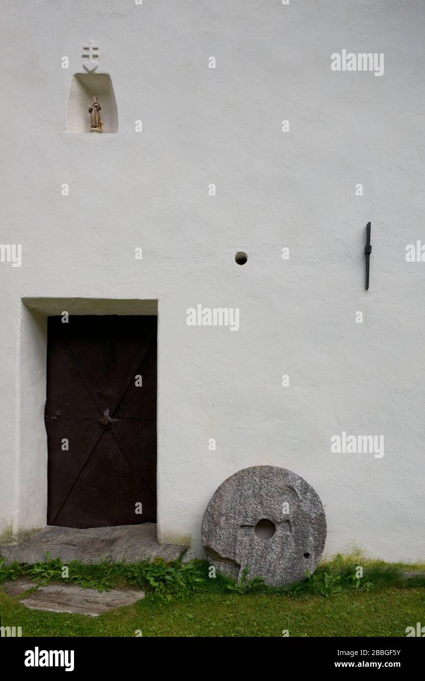 Detail der weißen Wand des historischen bauernhauses aus österreich mit Mühlstein und Eisenklappe Stockfoto