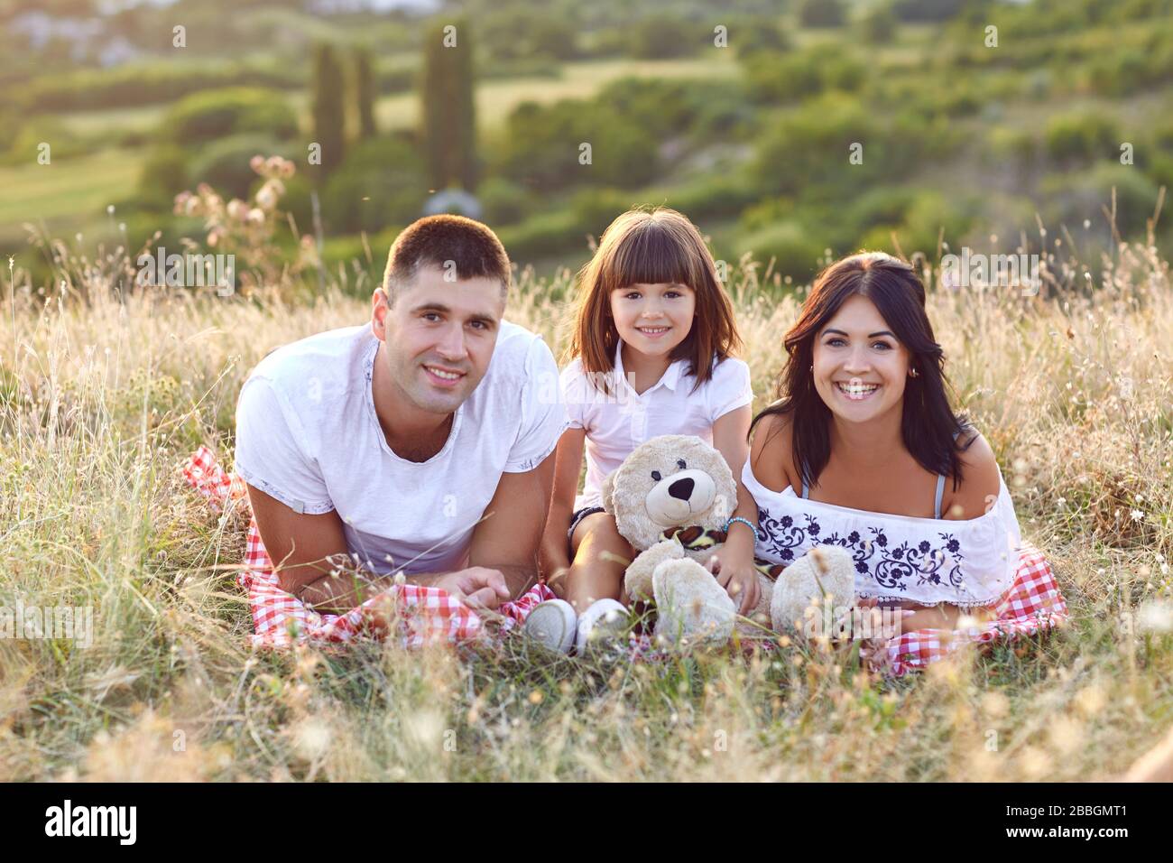 Glückliche Familie auf ein Picknick im Freien bei Sonnenuntergang. Mutter, Vater und Tochter in Ruhe gemeinsam in der Natur nicht. Stockfoto Glückliche Familie auf ein Picknick im Freien bei Sonnenuntergang. Mutter, Vater und Tochter in Ruhe gemeinsam in der Natur nicht. Stockfoto