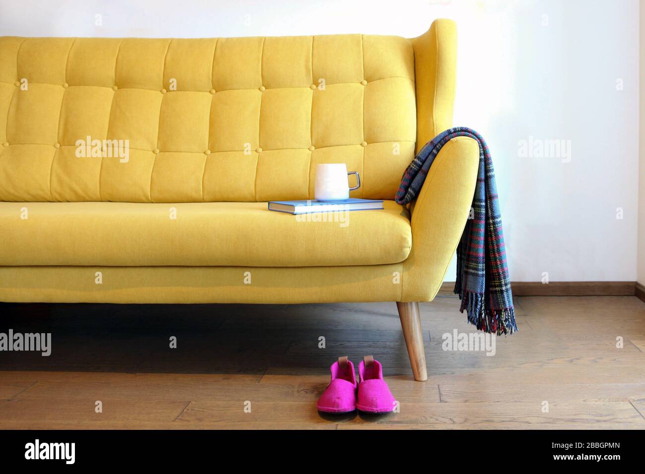 Tasse Tee und blaues Buch auf einem gelben Trainer. Details zum Stillleben im Inneren des Wohnzimmers. Gemütliches Innenleben, Komfortkonzept für zu Hause, frei von Geschlecht Stockfoto